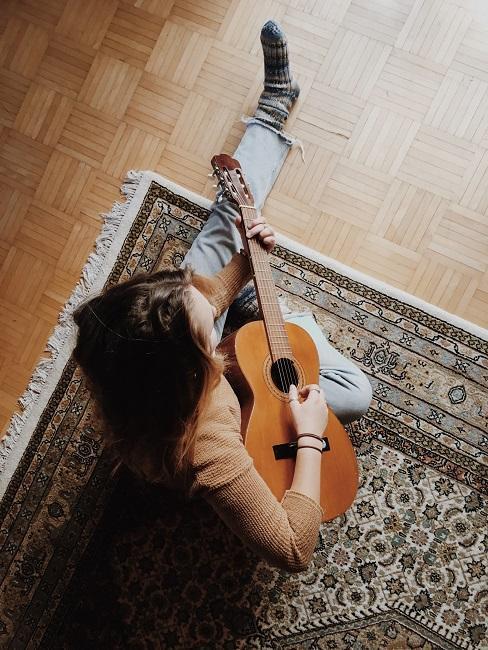 Osoba siedząca na dywanie grająca na gitarze
